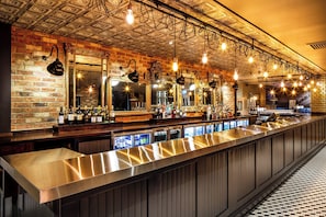 Un bar avec un long comptoir, de nombreux miroirs, des ampoules suspendues et un mur en briques.