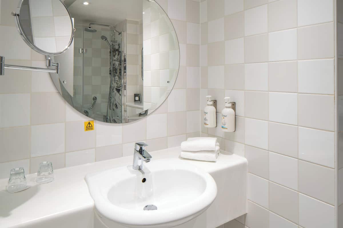 A bathroom with a sink, mirror, and shower.
