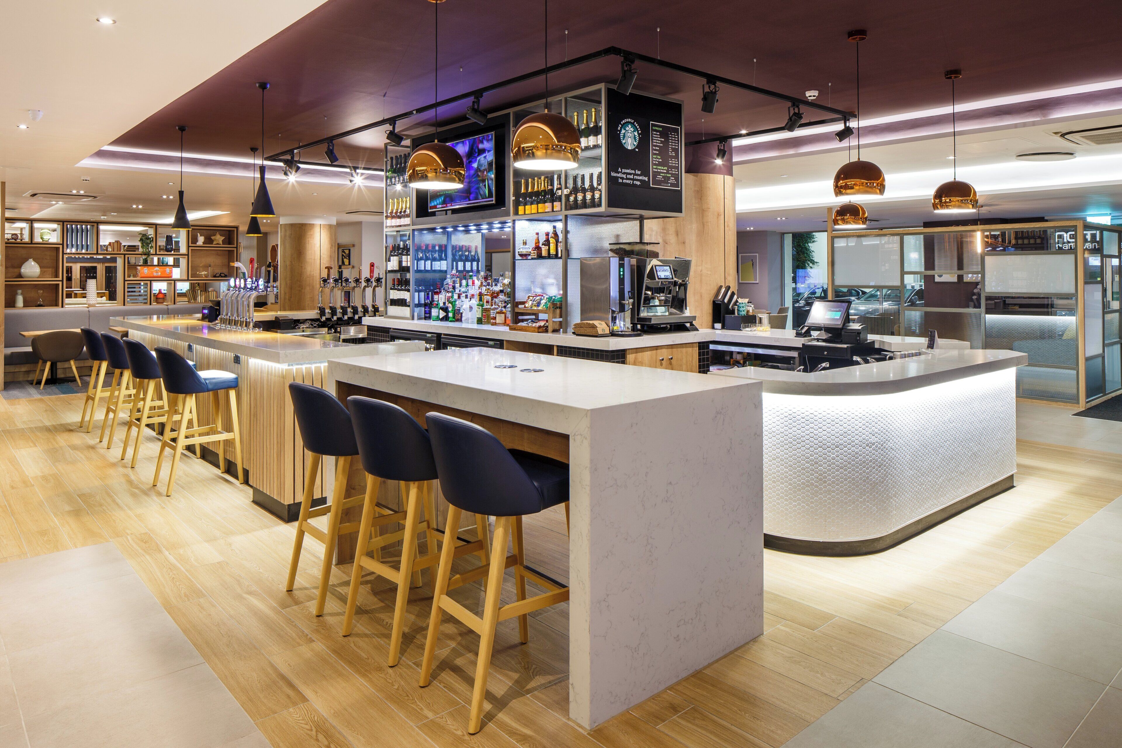 Un espace bar moderne comprenant un comptoir, des tabourets et une variété de bouteilles et de verres.