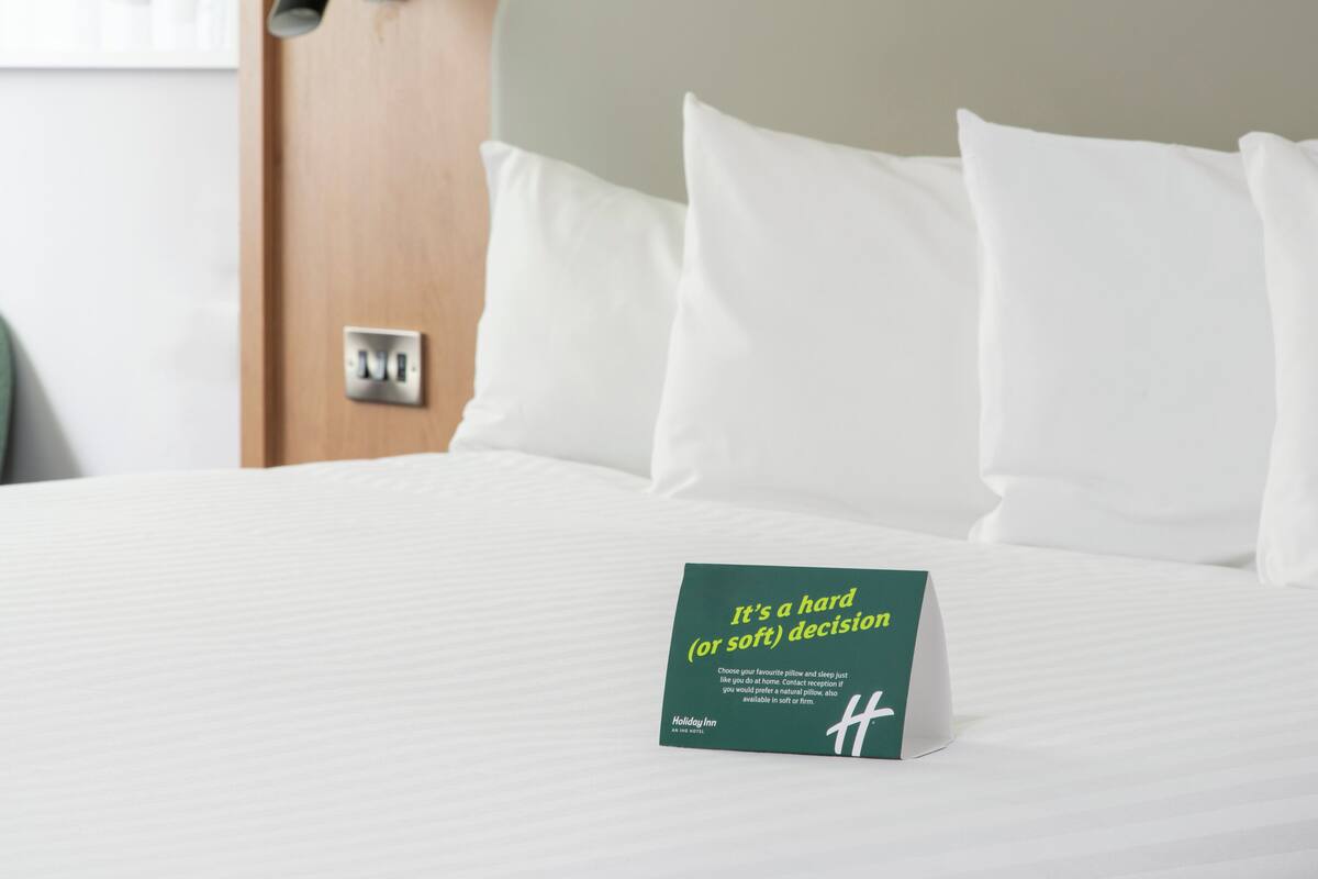 Un lit bien fait, avec du linge de lit blanc et une carte proposant différents types d’oreillers posée dessus.