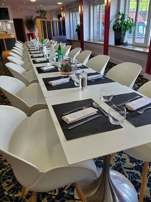 A conference room with white chairs, black placemats, and a long table set for a meeting.