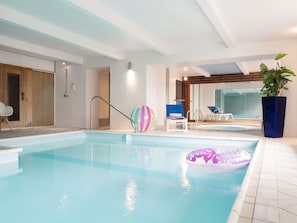 An indoor swimming pool with clear water, a lounge area with chairs, and a large potted plant. - Mercure Epinal Centre (Epinal)