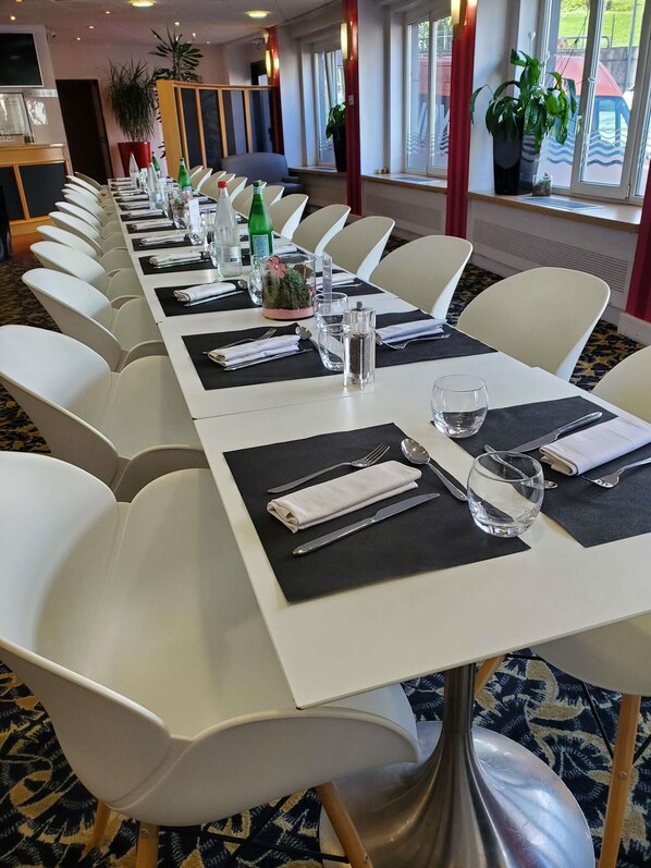 A conference room with white chairs, black placemats, and a long table set for a meeting.