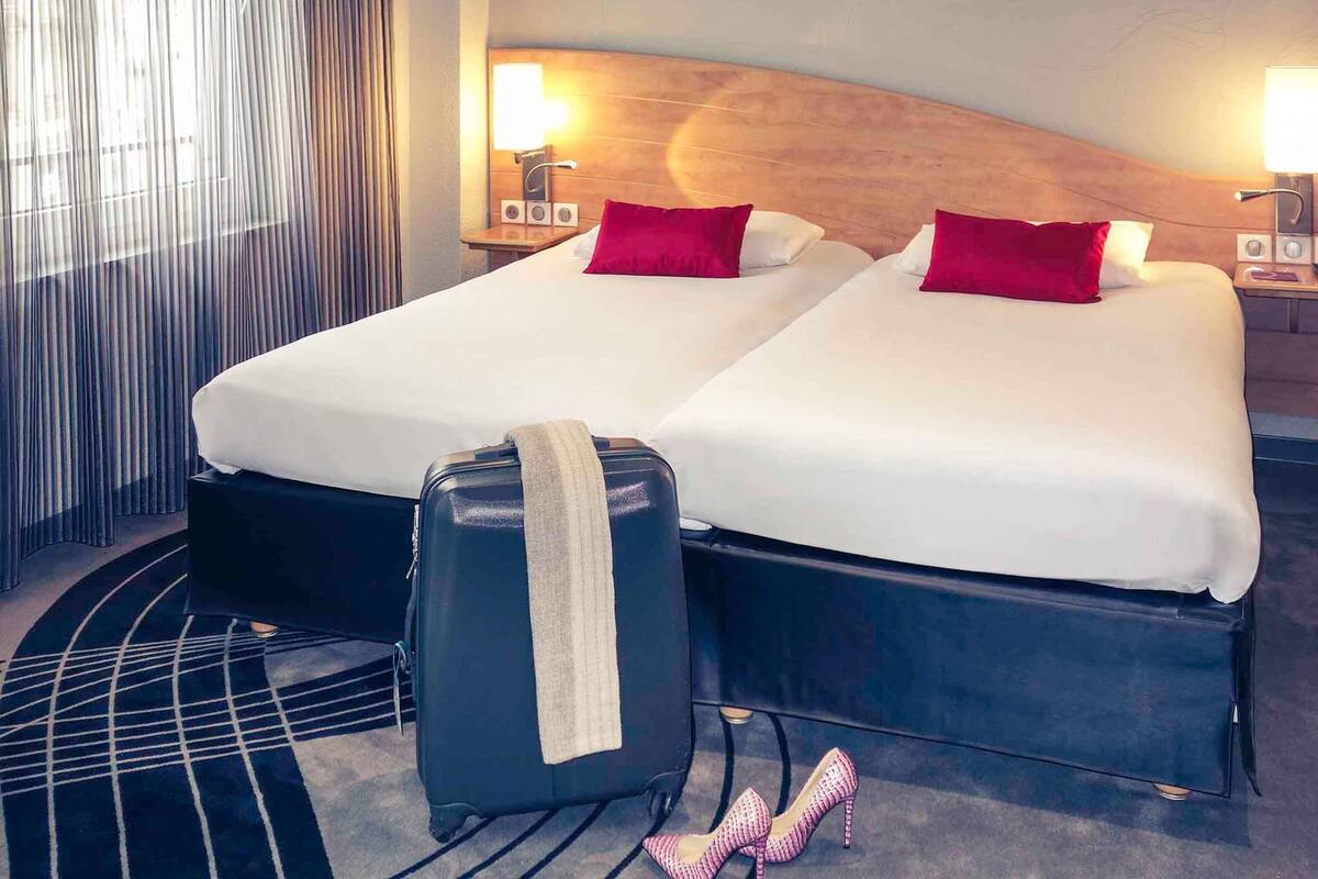 A hotel room with two beds, a suitcase, and a pair of high heels.