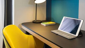 A laptop on a desk with a book, a lamp, and a yellow chair.