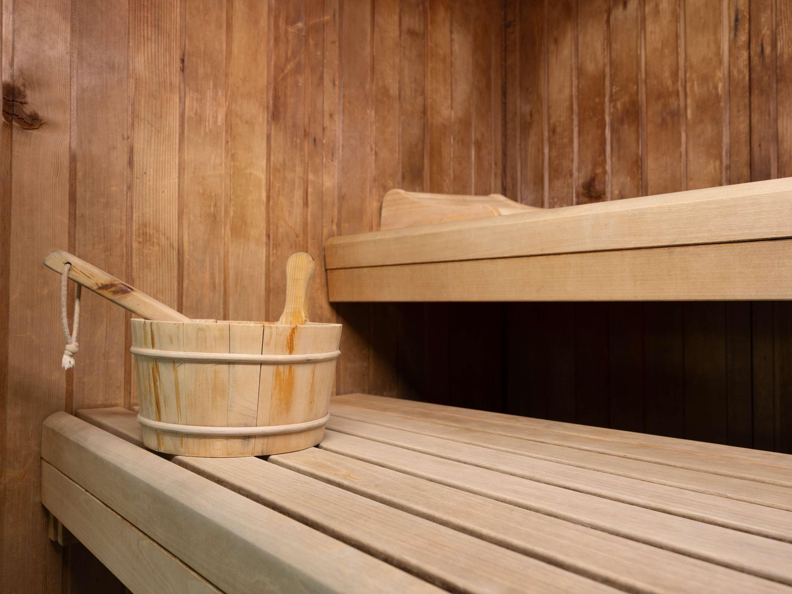 Una sauna con un banco de madera y un balde de madera con un mortero.