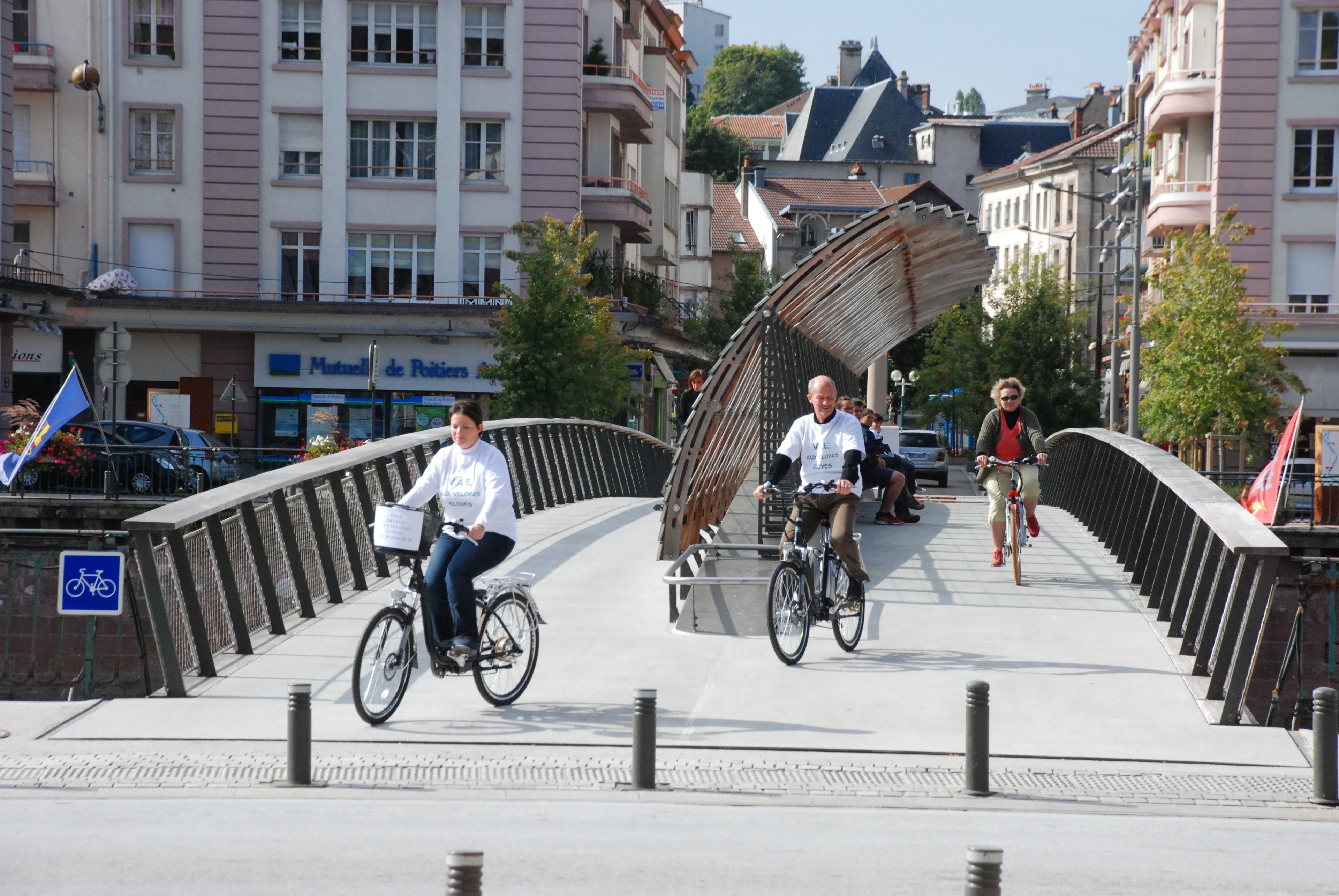 A pedestrian bridge with a curved metal railing, surrounded by buildings with balconies and storefronts.
