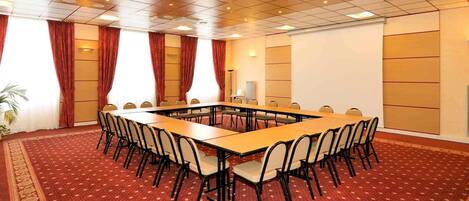 A conference room with a long table, chairs, a patterned carpet, and a ceiling with recessed lighting.