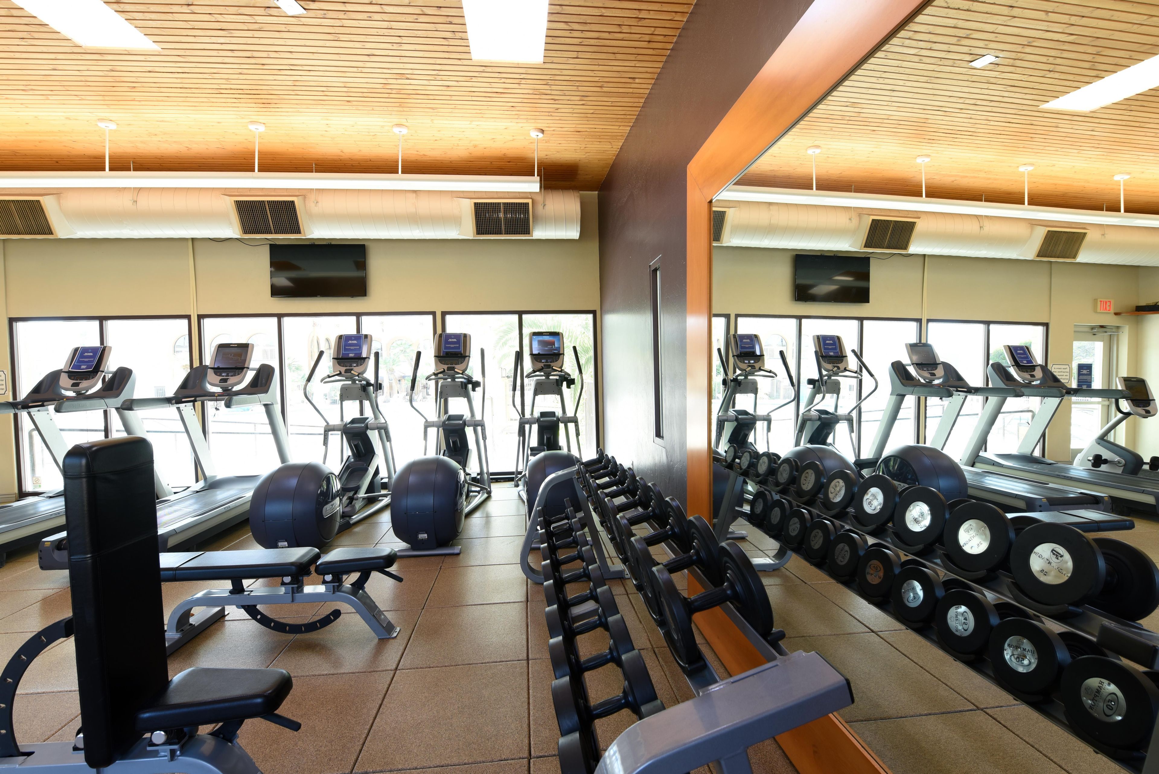 Une salle de sport équipée de divers appareils d’exercice, notamment des tapis de course, des vélos elliptiques et des bancs de musculation.