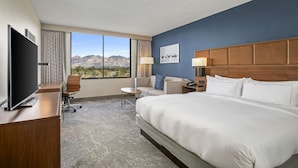Habitación de hotel con una cama grande, un escritorio con televisor, un sofá y vistas a las montañas.