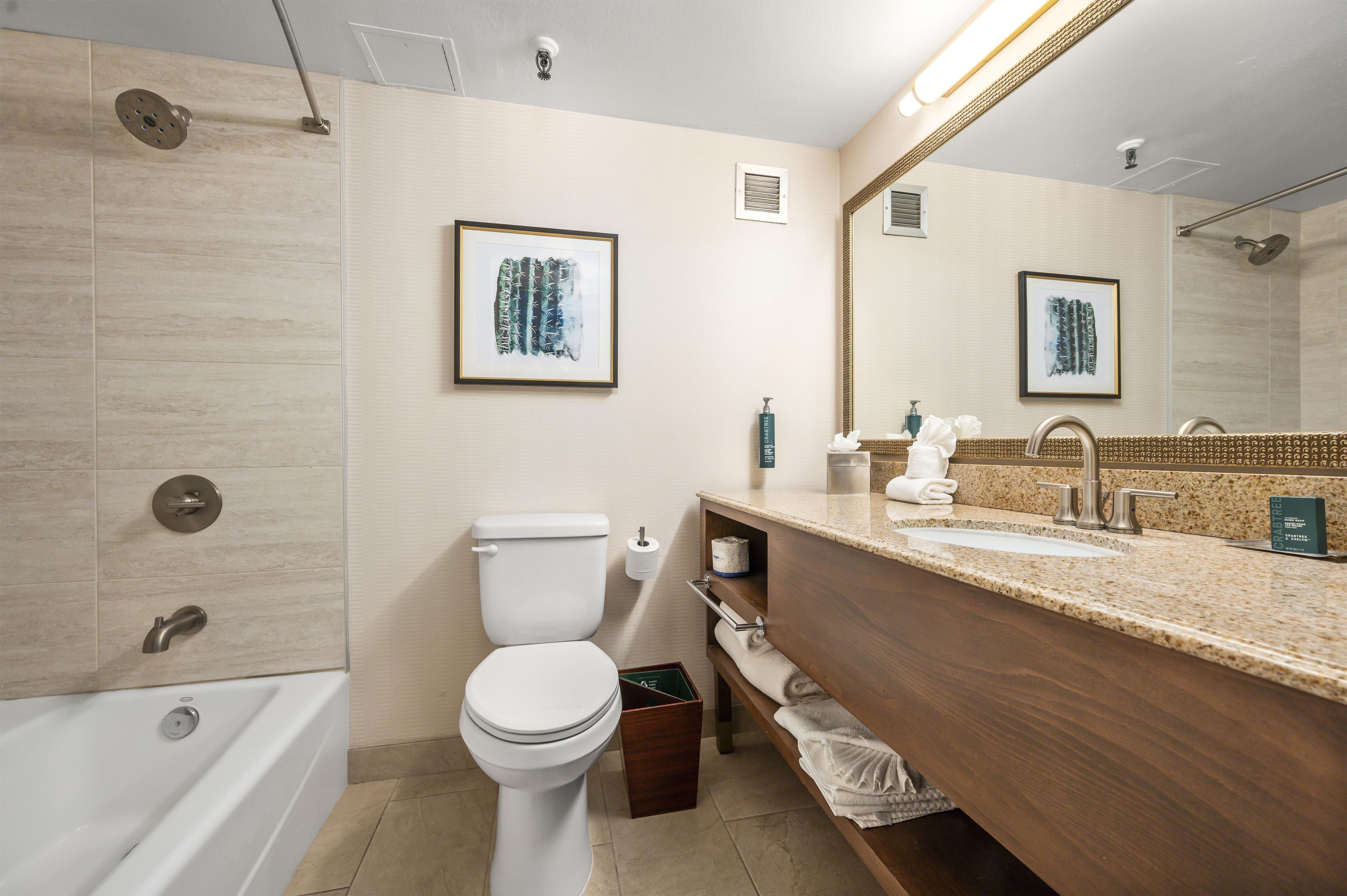A modern bathroom with a bathtub, toilet, and sink. There are framed artworks on the wall, a towel rack, and a mirror above the sink.