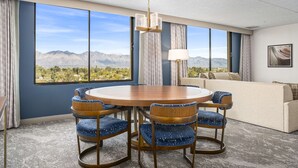 Una habitación con una mesa redonda, sillas tapizadas en azul, un sofá y vistas a montañas.