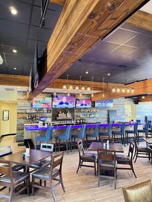 A bar area with multiple screens, a counter with a blue top, and several chairs and tables. - DoubleTree by Hilton Tucson - Reid Park (Tucson)