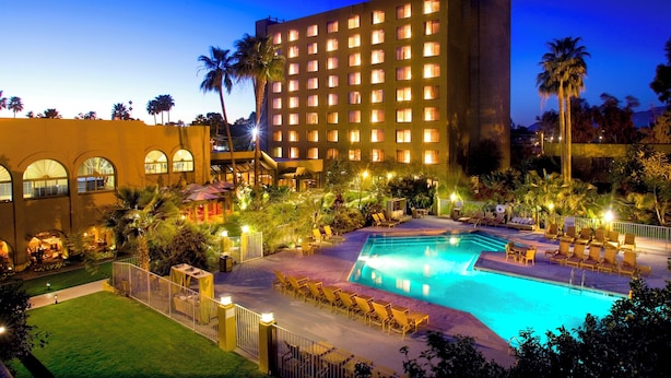 Un hotel con piscina, palmeras y un edificio grande con ventanas iluminadas.