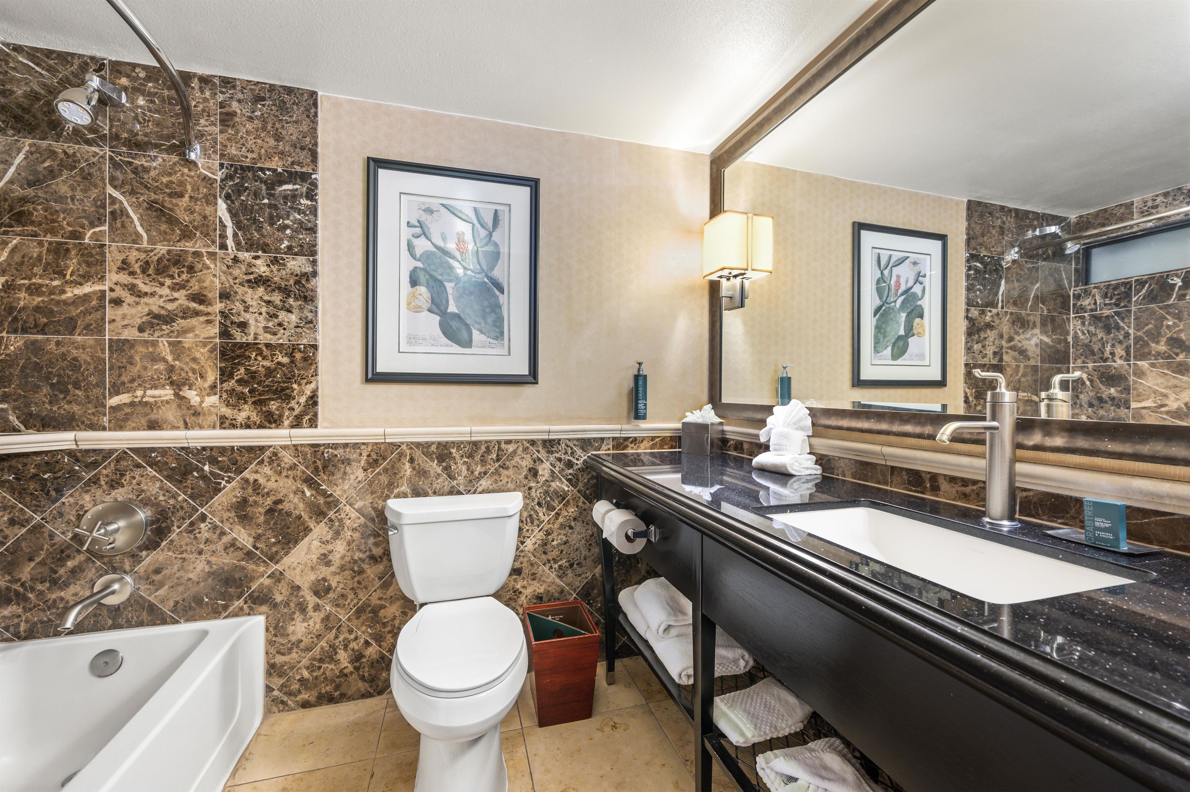 A bathroom with a toilet, sink, and shower. There are framed botanical prints on the wall.
