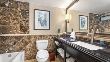 A bathroom with a toilet, sink, and shower. There are framed botanical prints on the wall.