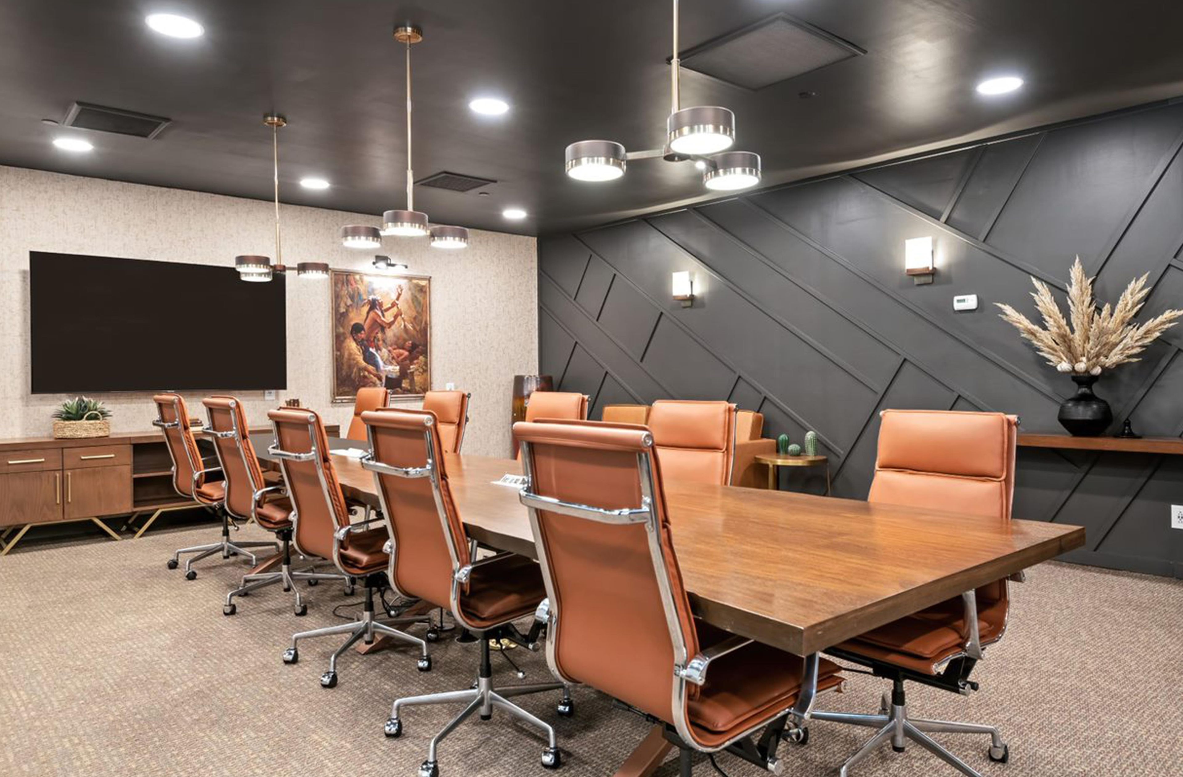 A conference room with a long table, leather chairs, a large screen, and modern lighting fixtures.