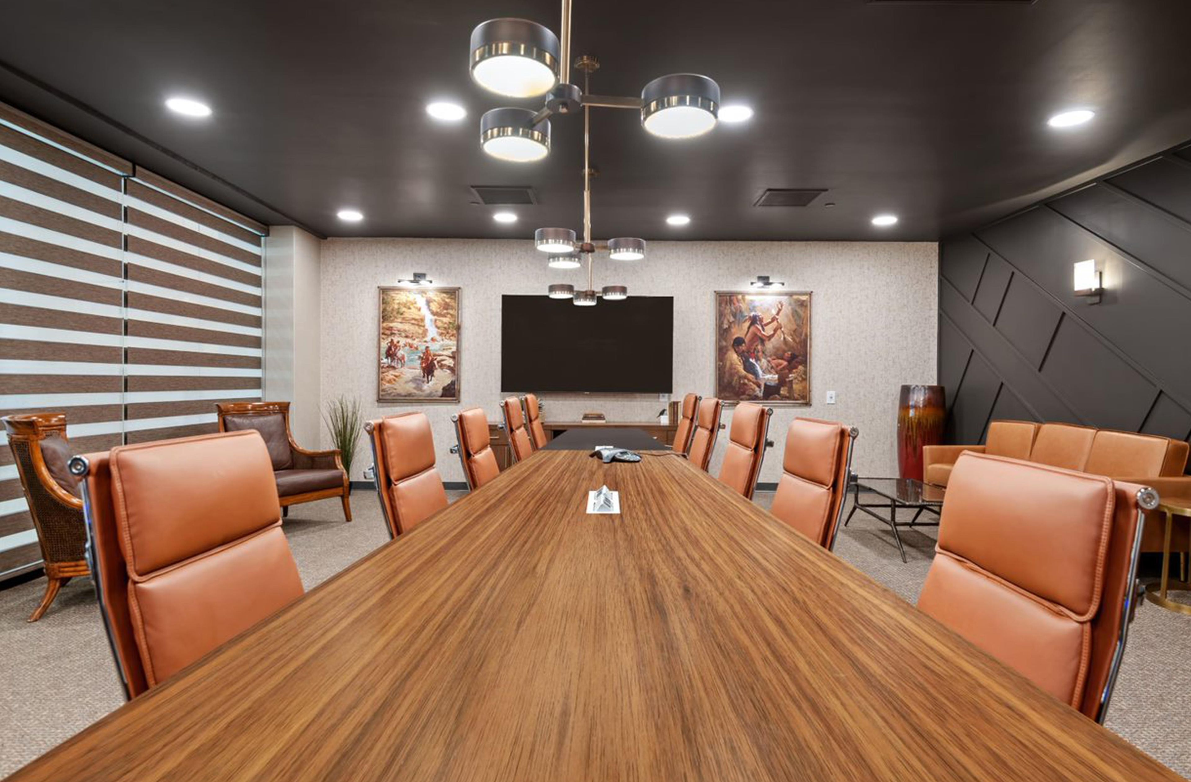 A conference room with a long wooden table, leather chairs, a large flat-screen TV, and artwork on the walls.