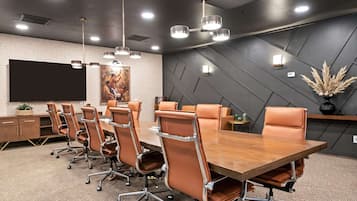 A conference room with a long table, multiple chairs, a large screen, and modern lighting fixtures.