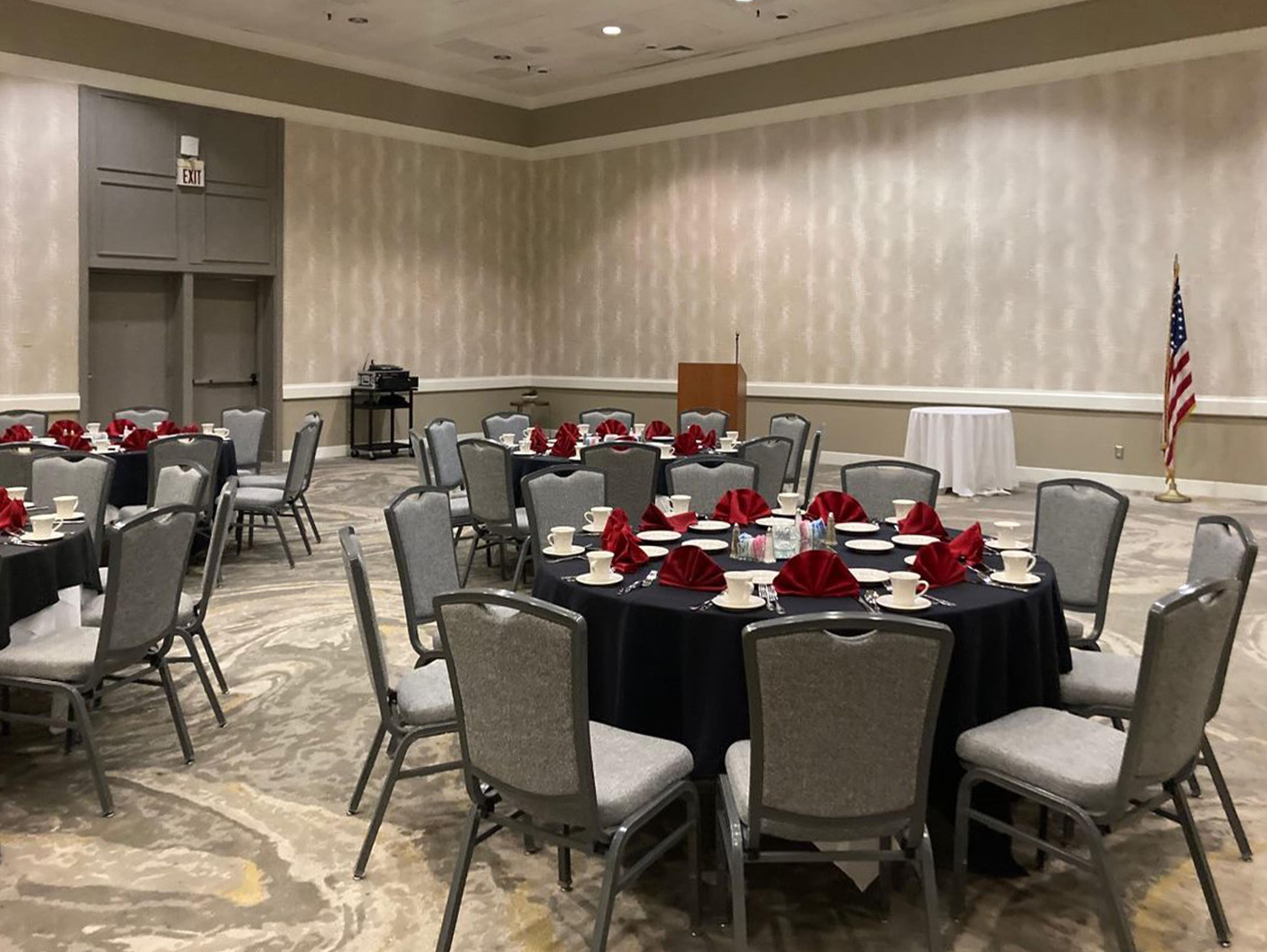 A conference room with round tables, grey chairs, and red napkins.