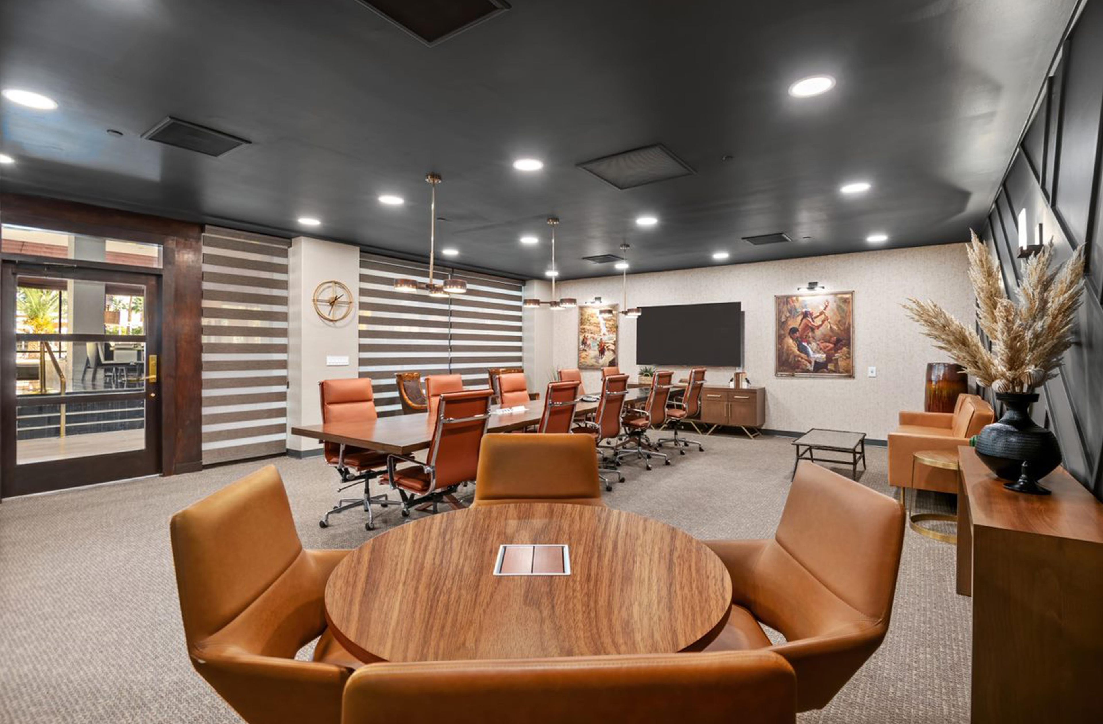 A conference room with a round table, multiple chairs, a large screen, and a clock on the wall.