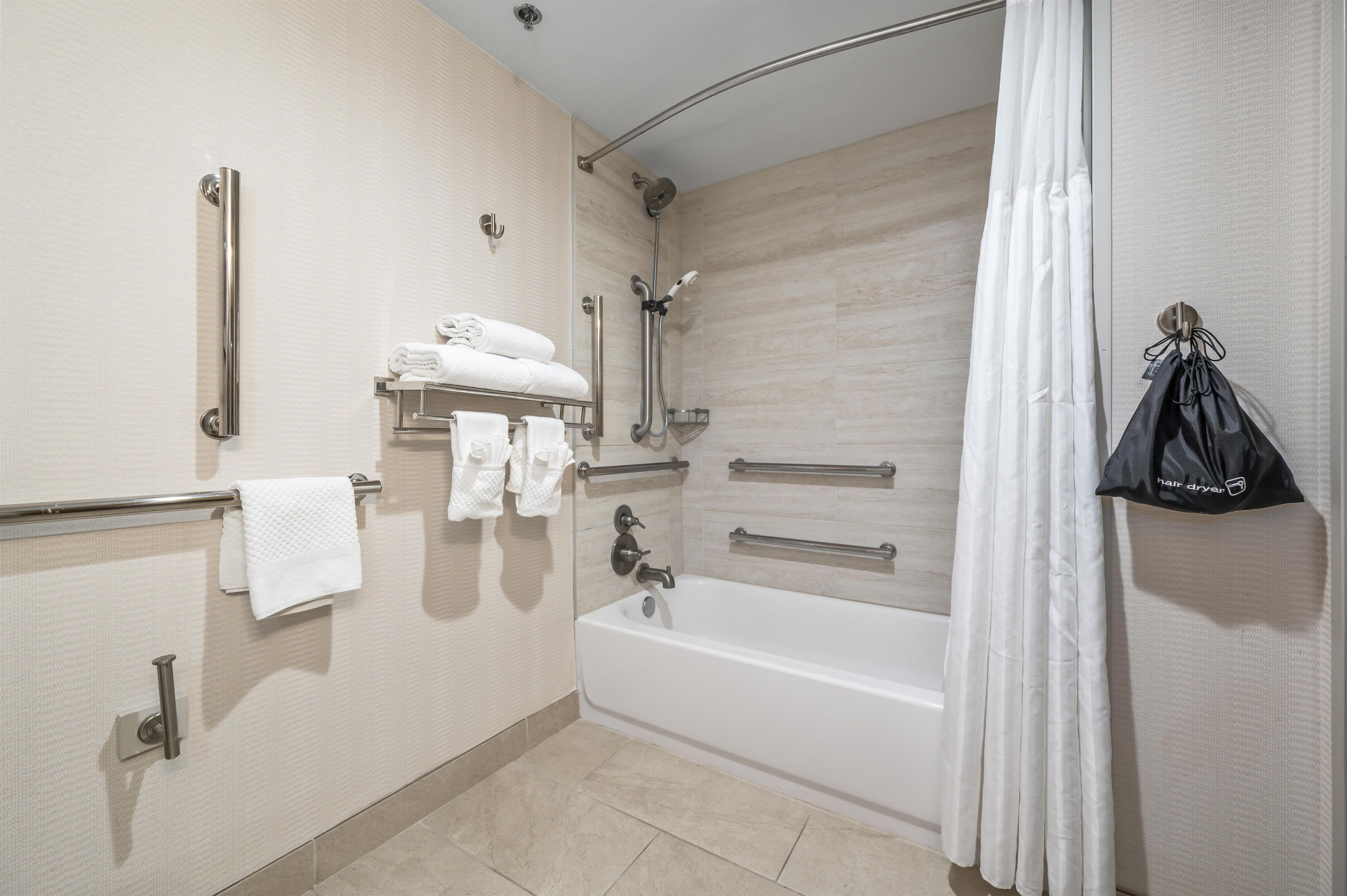 A modern bathroom with a bathtub, shower, and handrails.