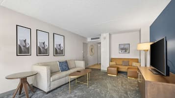 Una sala de estar moderna con un sofá color beige, una mesa de centro redonda, un televisor sobre un mueble de madera y cuadros enmarcados en la pared.