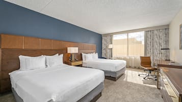 A hotel room with two beds, a desk, a chair, and a large window with curtains.
