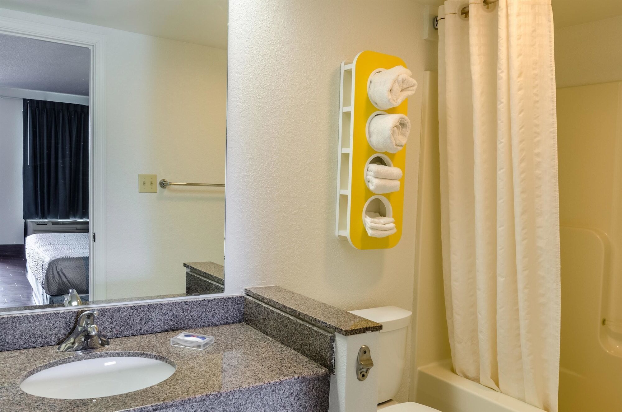 A bathroom with a granite countertop sink, a toilet, and a towel rack with three towels.