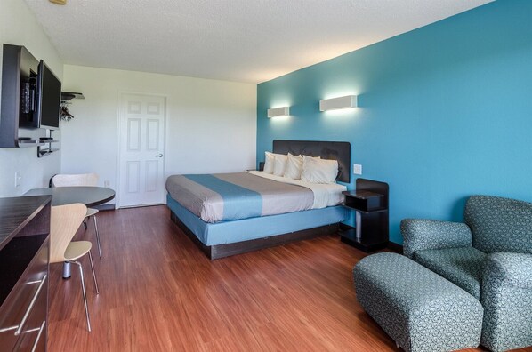 A modern hotel room with a bed, a desk, and a seating area.