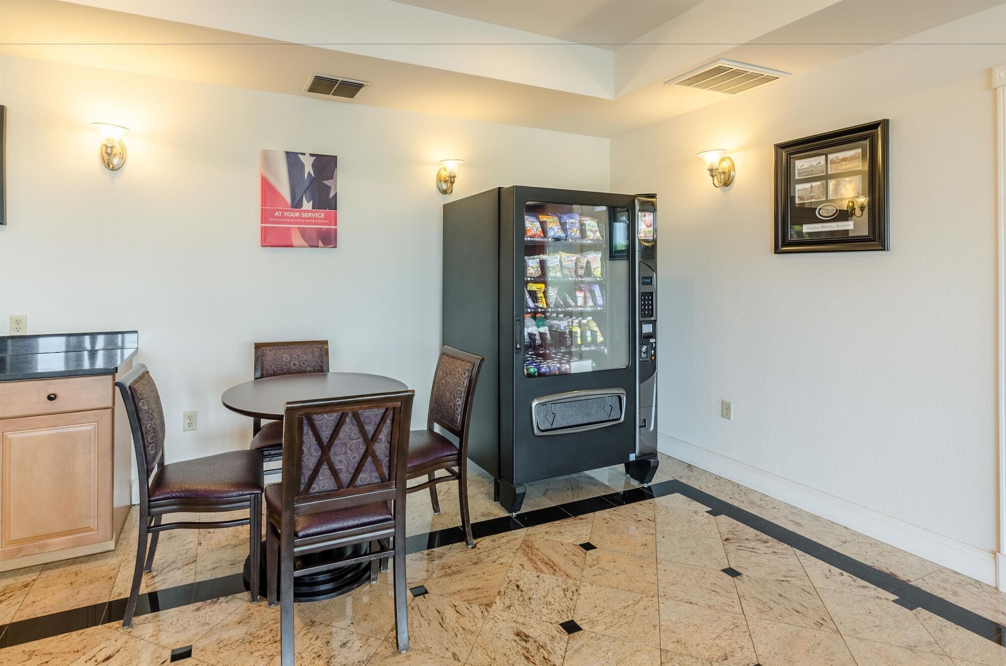 A hotel room with a dining area, a vending machine, and a framed picture on the wall.
