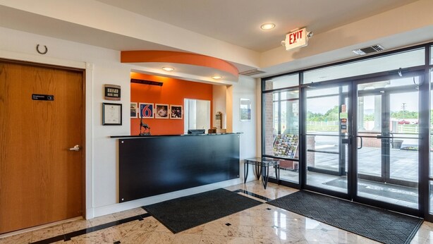 A reception area with a wooden door, a black reception desk, and a glass door leading outside. - Motel 6 Lexington, VA (Lexington)