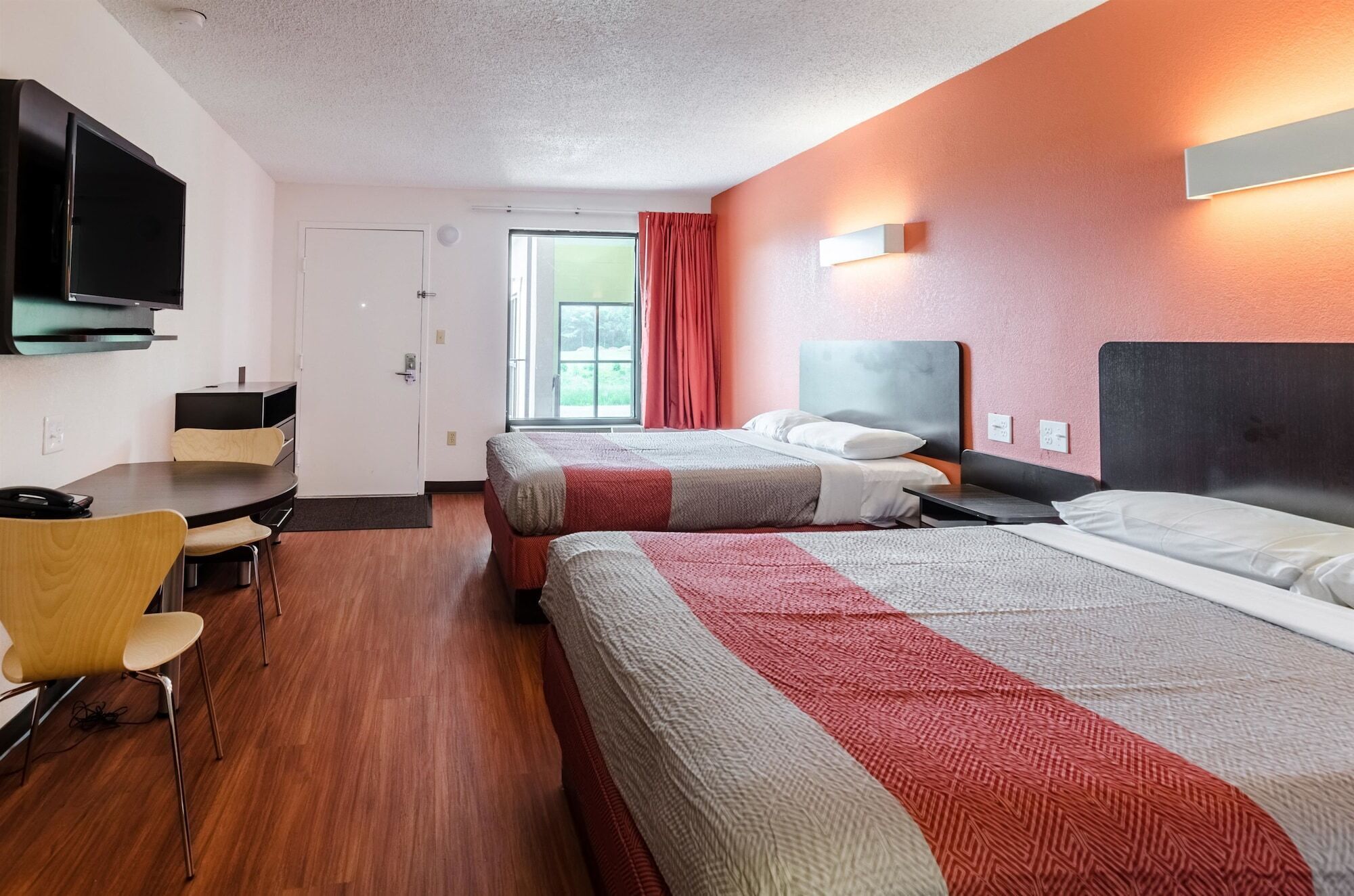 A hotel room with two beds, a desk, and a TV.