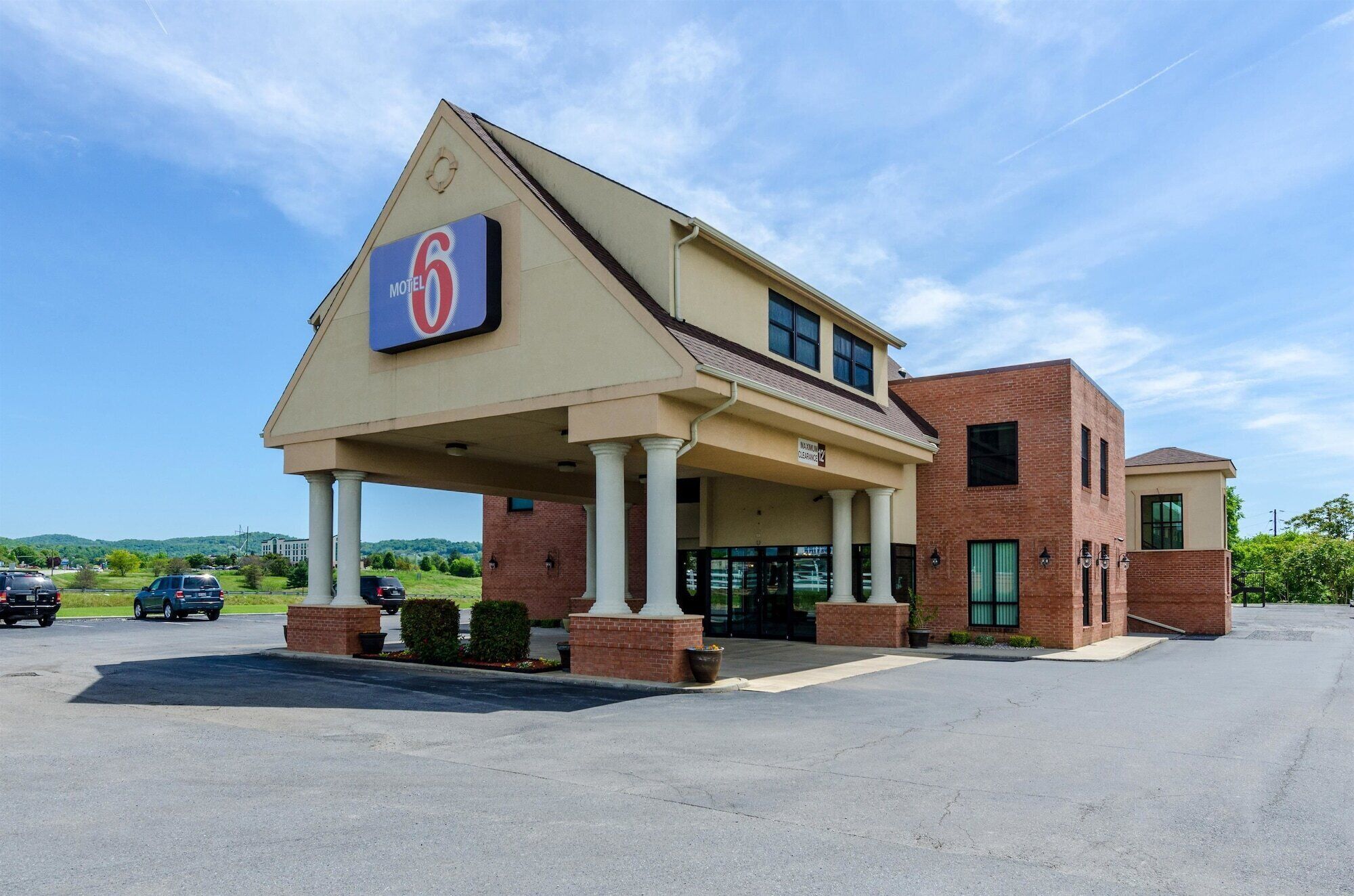 Edificio de Motel 6 con un letrero grande, entrada cubierta y estacionamiento.