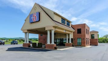 Edificio de Motel 6 con un letrero grande, entrada cubierta y estacionamiento.