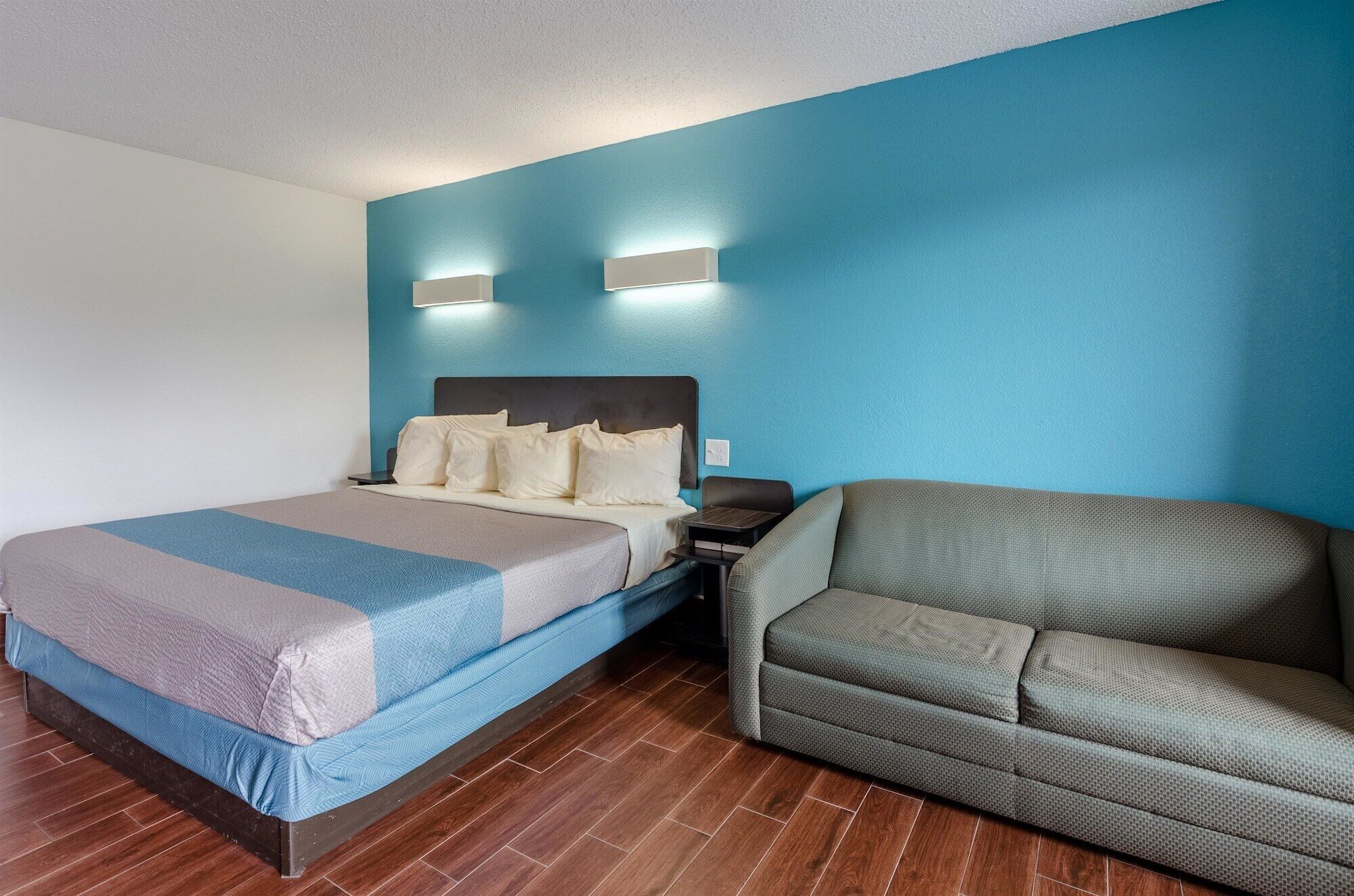 A hotel room with a bed, a nightstand, a sofa, and two wall-mounted lights.