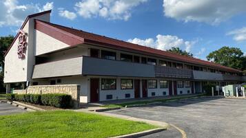 A motel with a red roof, multiple rooms, and a parking lot.