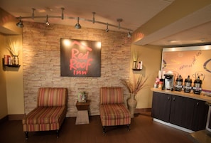 A Red Roof Inn reception area with two striped armchairs, a coffee station, and a stone wall backdrop. - Red Roof Inn Lafayette, LA (Lafayette)
