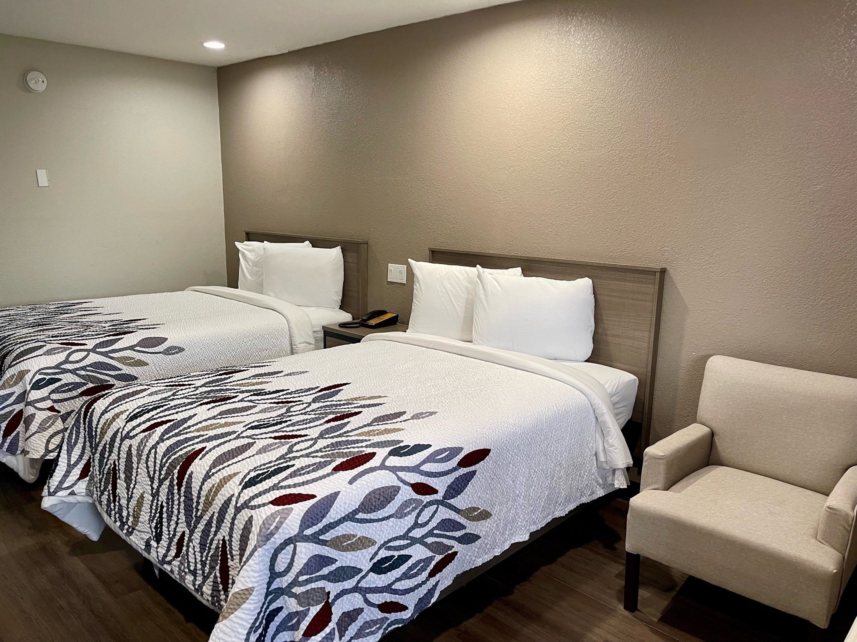Quarto de hotel com duas camas, uma cadeira e uma mesa de cabeceira com telefone.