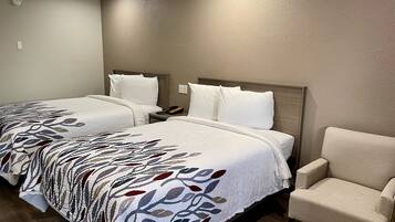 Quarto de hotel com duas camas, uma cadeira e uma mesa de cabeceira com telefone.