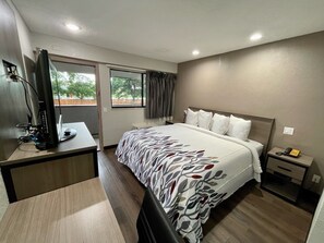 A hotel room with a bed, a desk with a computer, a television, a window with curtains, and a nightstand with a phone. - Red Roof Inn Lafayette, LA (Lafayette)
