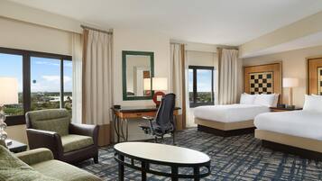 Een hotelkamer met een bureau, twee bedden, een stoel, een ronde tafel en uitzicht op de stad.