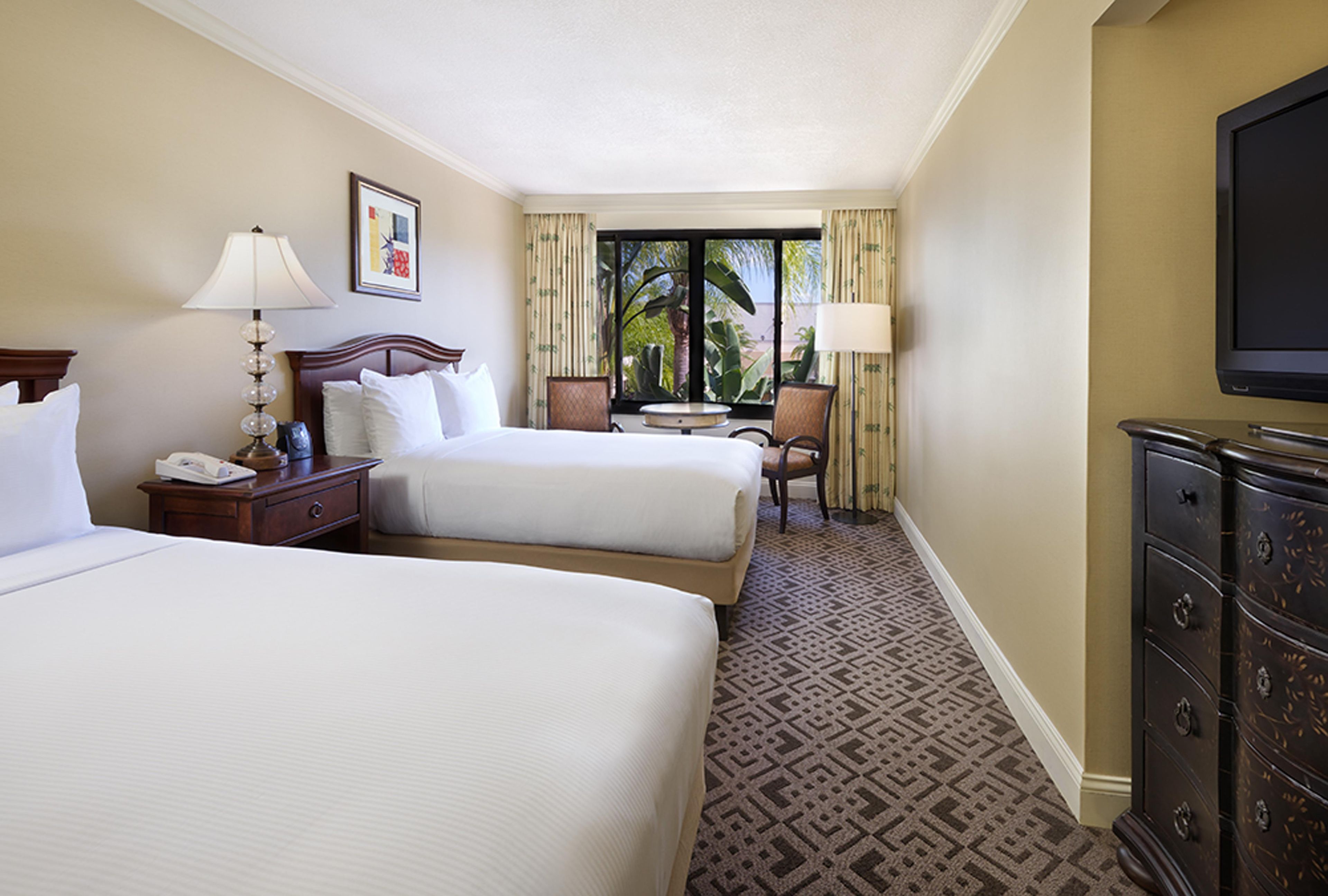 A hotel room with two beds, a desk, a chair, a television, and a window with curtains.