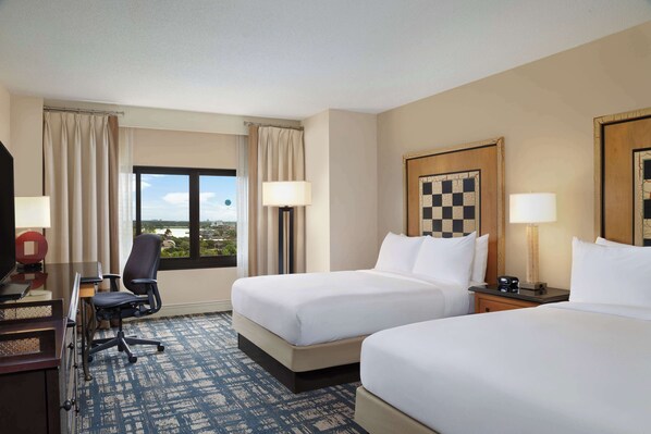 A hotel room with two beds, a desk, a chair, a lamp, a clock, and a window with a view. - Hilton Orlando Lake Buena Vista - Disney Springs® Area (Lake Buena Vista)