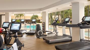 A gym with treadmills, stationary bikes, and a pool area visible through large windows.