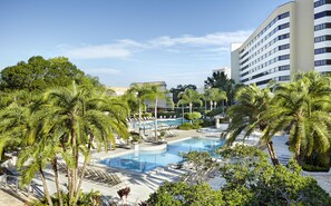 A resort pool area with palm trees, lounge chairs, and a modern building in the background. - Hilton Orlando Lake Buena Vista - Disney Springs® Area (Lake Buena Vista)