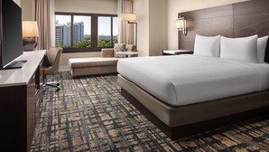 A hotel room with a large bed, a desk, a chair, a small table, and a view of the cityscape. - Hilton Orlando Lake Buena Vista - Disney Springs® Area (Lake Buena Vista)