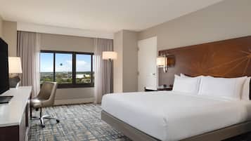 Quarto de hotel com uma cama grande, uma escrivaninha, uma cadeira, uma janela com vista e uma mesa de cabeceira.