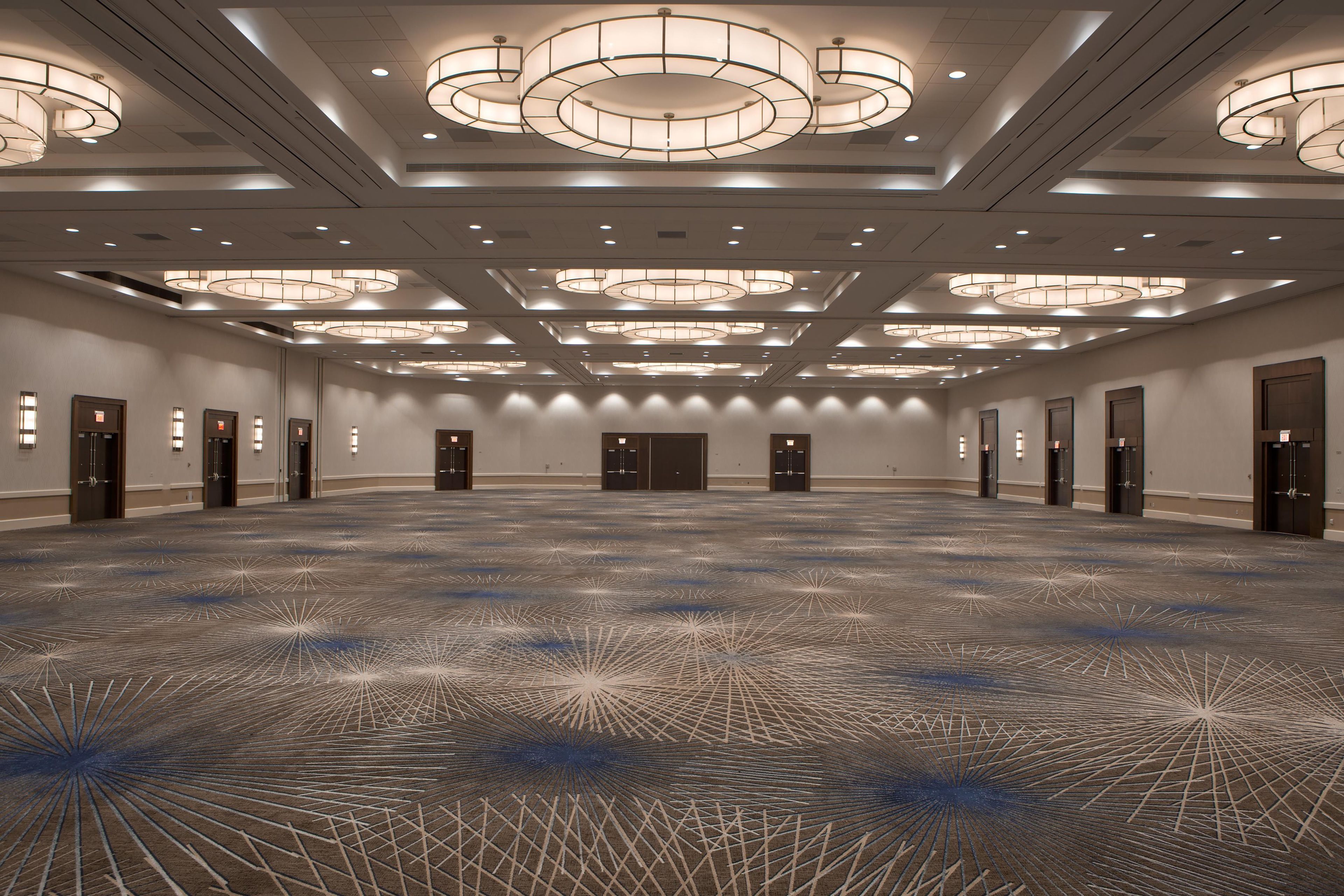 A spacious conference room with a patterned carpet, multiple doors, and a ceiling with circular light fixtures.