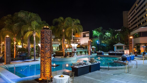 A pool area with multiple pools, lounge chairs, and a dining setup. - Hilton Orlando Lake Buena Vista - Disney Springs® Area (Lake Buena Vista)